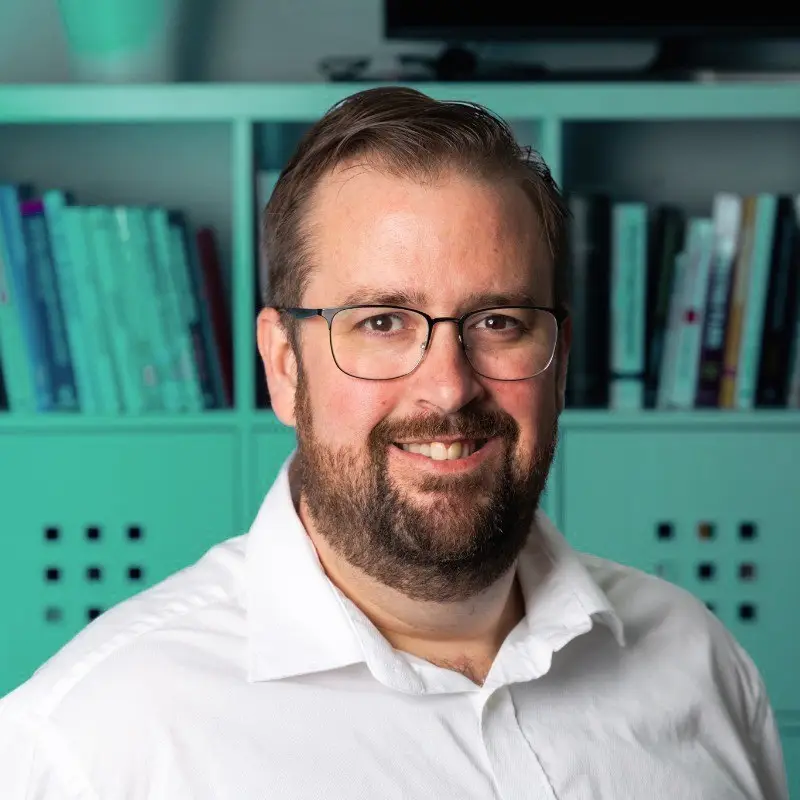 Chris, smiling, in front of teal bookshelves