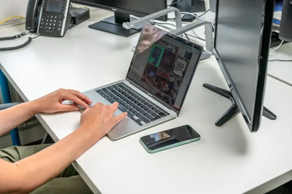 Hands on a laptop showing a grid of social media posts